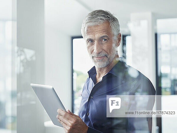 Smiling mature businessman with tablet PC seen through glass