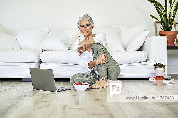 Woman with laptop and bowl of strawberries at home