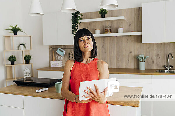 Thoughtful woman with tablet PC standing in kitchen at home