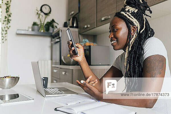 Smiling businesswoman using smart phone by laptop at home