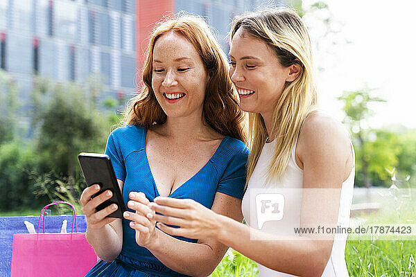Smiling friends using smart phone in city