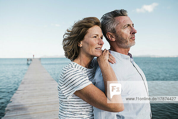 Smiling mature woman with hands on man's shoulder at jetty