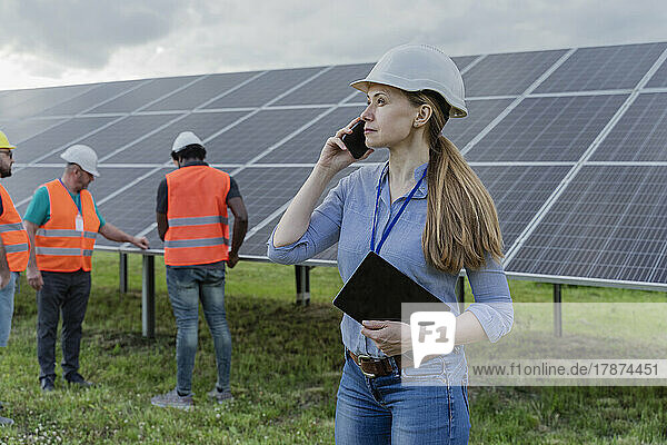 Woman talking on mobile phone with coworkers in background at solar station