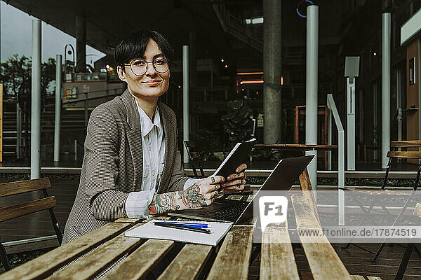 Smiling businesswoman with diary and laptop sitting at table