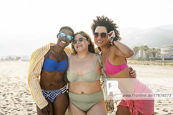 Smiling women wearing sunglasses with arms around at beach