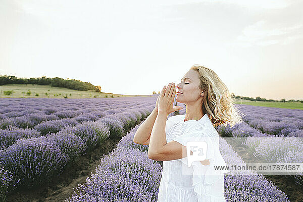 Smiling woman with hands clasped praying in lavender field