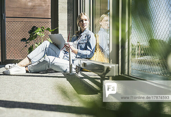 Businesswoman with tablet PC and wind turbine model sitting in office on sunny day