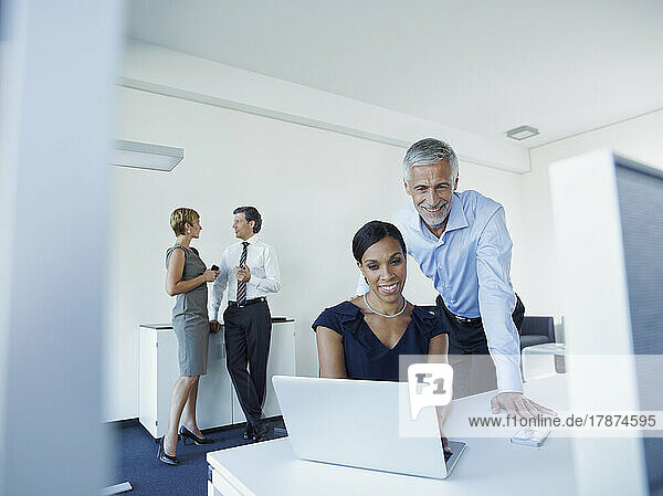 Smiling businesswoman and businessman using laptop with colleagues discussing in office