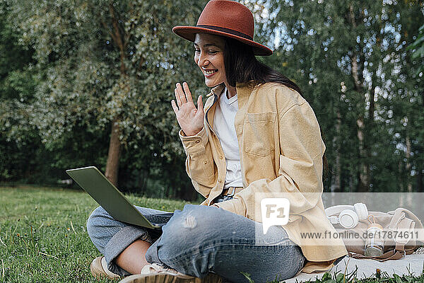 Smiling woman waving on video call through laptop at park