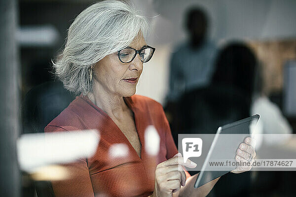 Senior businesswoman using tablet PC seen through glass window