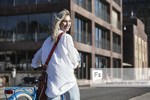 Smiling young woman walking with bicycle on sunny day