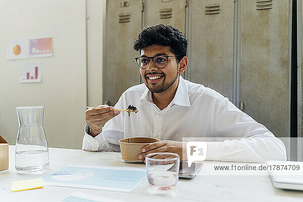 Smiling businessman with eyeglasses eating lunch at office
