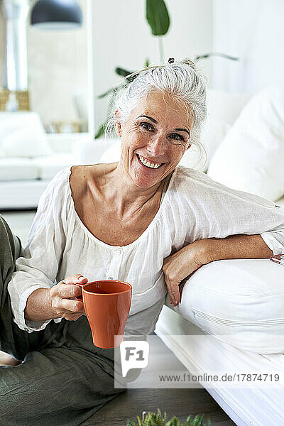 Smiling woman holding coffee mug leaning on couch