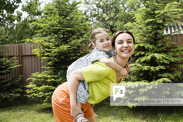 Happy mother giving backpack ride to daughter at backyard