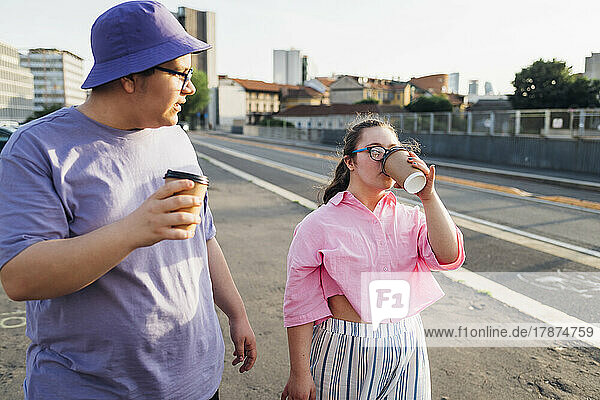 Teenage girl with down syndrome drinking coffee by brother on street in city