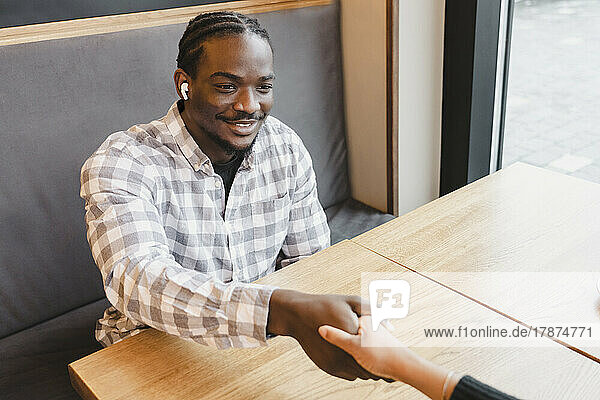 Happy young businessman shaking hand with businesswoman at cafe