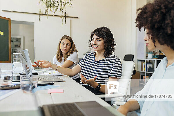 Smiling businesswoman gesturing in meeting by colleagues at office