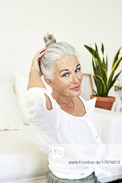 Smiling woman tying hair bun sitting at home