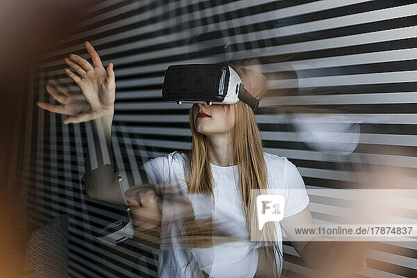 Teenage girl wearing virtual reality headset gesturing by striped wall