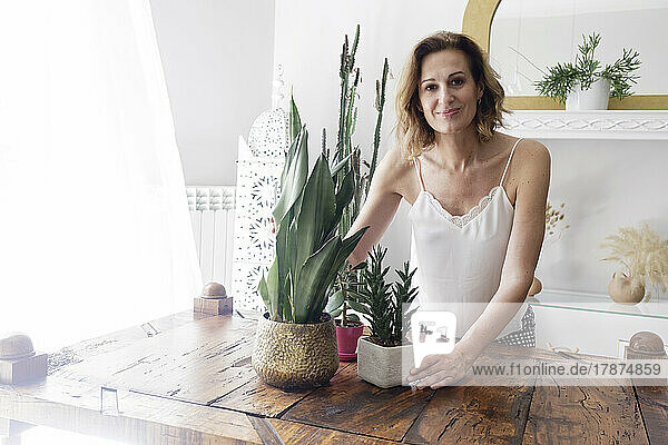 Smiling woman with potted plants on table at home