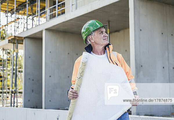 Thoughtful contractor with plan standing at construction site