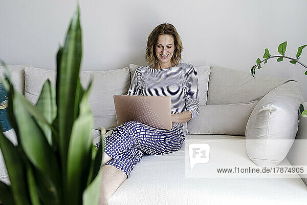 Smiling woman using laptop sitting on couch at home