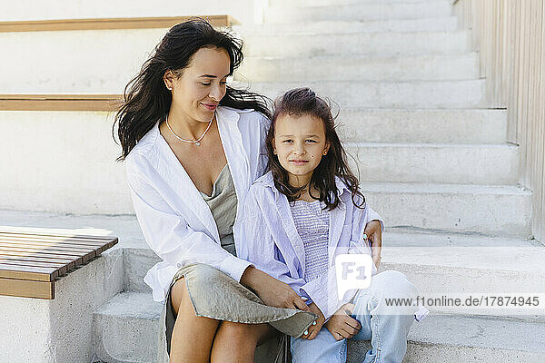 Lächelnde Frau mit Tochter  die auf Stufen sitzt