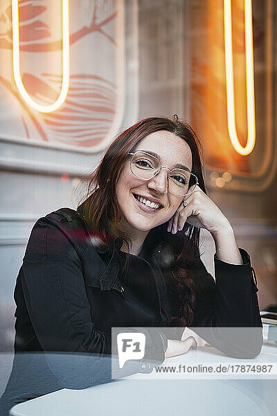 Glückliche junge Frau mit Brille sitzt am Tisch im Café