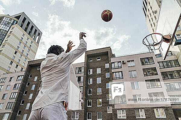 Man throwing basketball in hoop in front of buildings