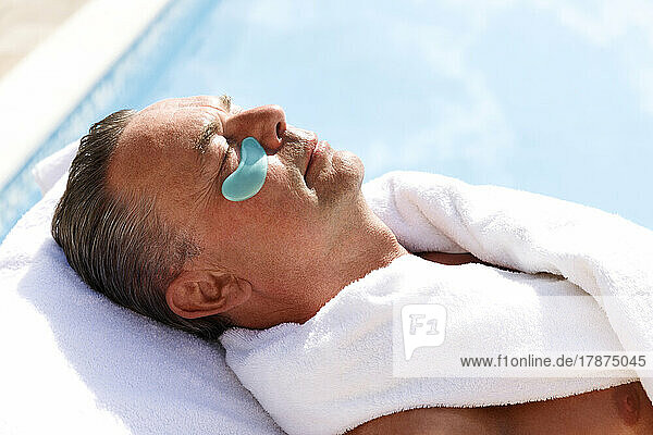 Mature man with collagen patch below eye at pool spa