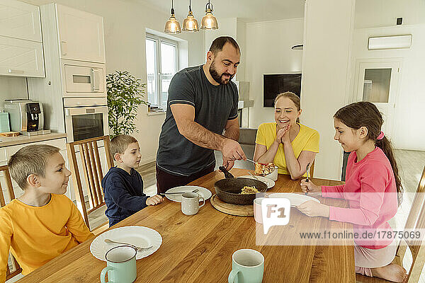 Lächelnder Vater serviert der Familie zu Hause Frühstück