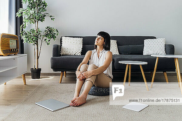 Thoughtful woman sitting on hassock at home