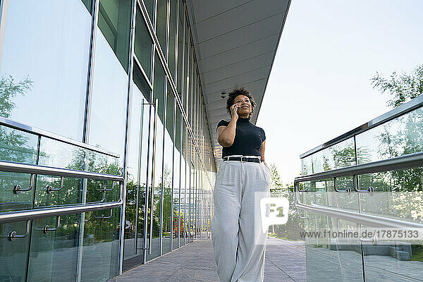 Young businesswoman talking on smart phone walking by office building