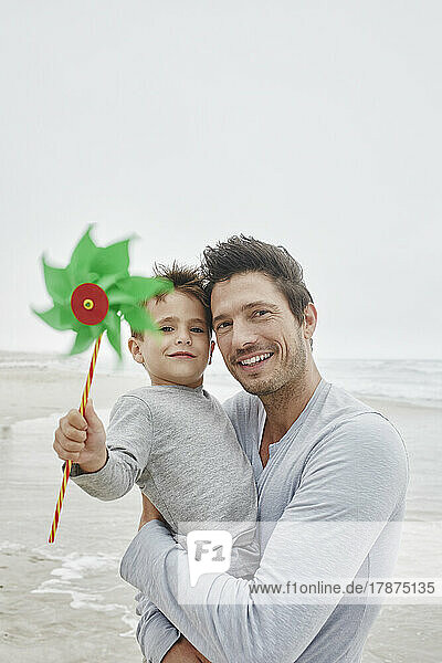 Father carrying son on the beach holding green pinwheel