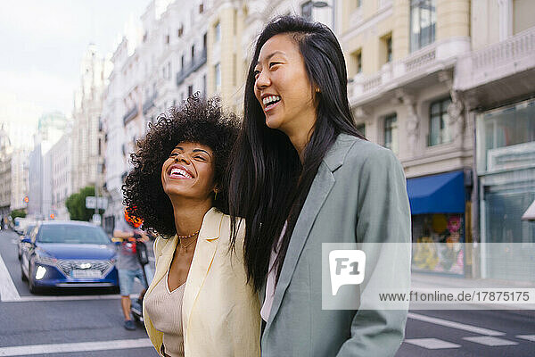 Cheerful multiracial friends crossing road in city