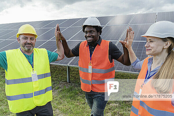 Smiling multiracial engineers giving high five to each other at solar power station