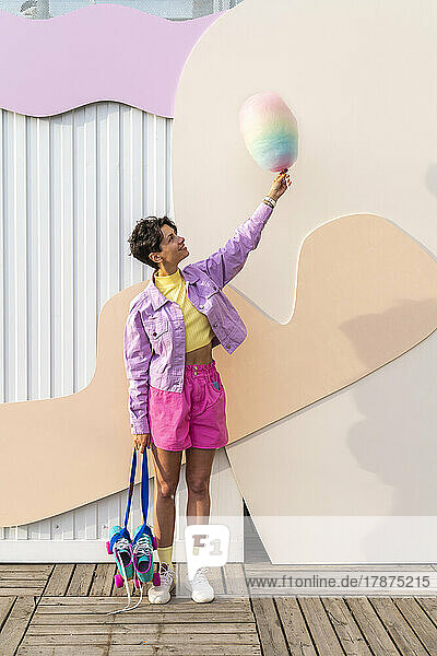 Smiling woman with roller skates holding cotton candy in front of wall