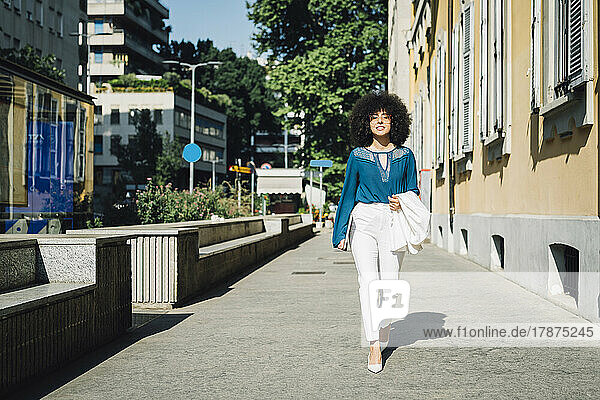 Businesswoman with laptop walking on sidewalk in city