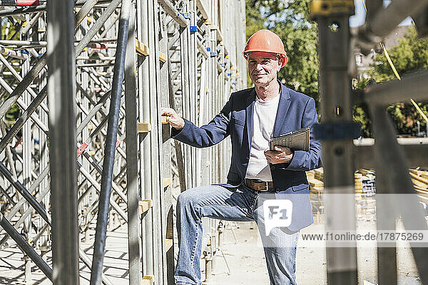 Smiling engineer with tablet PC standing by scaffolding