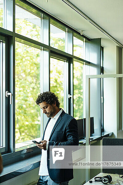 Businessman using mobile phone by window in office