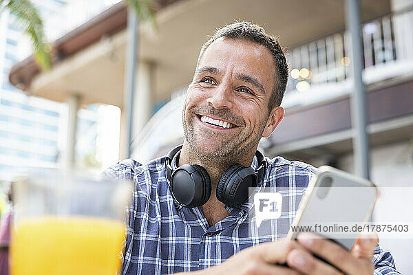 Happy mature man with smart phone and wireless headphones at cafe
