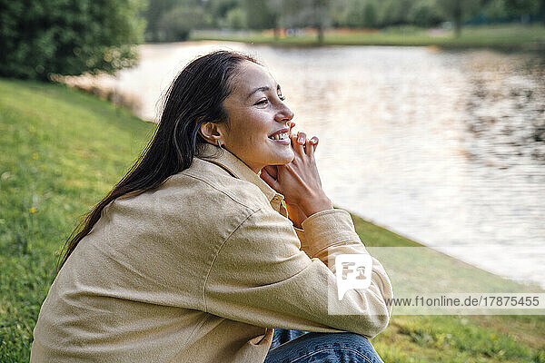 Smiling woman sitting by lake at park