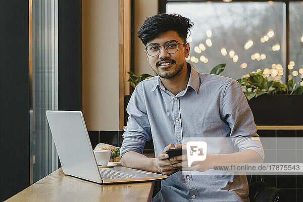 Happy freelancer with smart phone sitting at table in cafe