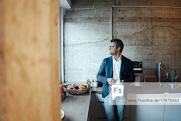 Mature businessman with coffee cup standing in office cafeteria