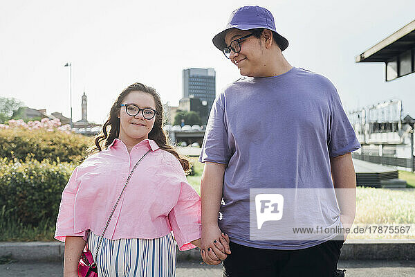 Teenage boy holding hand and looking at sister with down syndrome standing on footpath