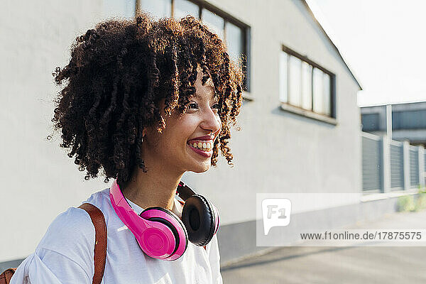 Happy young woman with curly hair wearing wireless headphones on sunny day