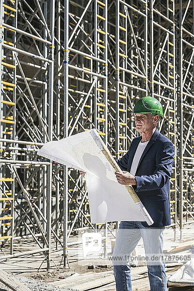 Architect examining blueprints standing in front of scaffolding