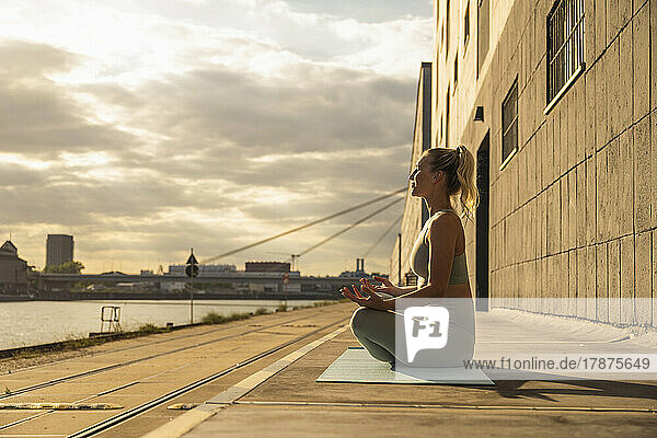 Young woman doing yoga on footpath at sunset