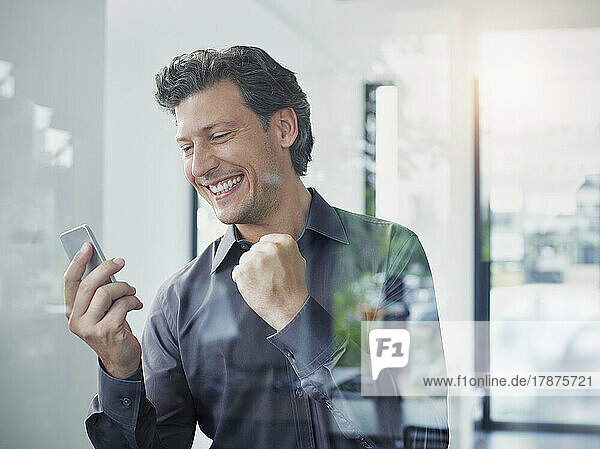 Successful businessman using smart phone seen through glass