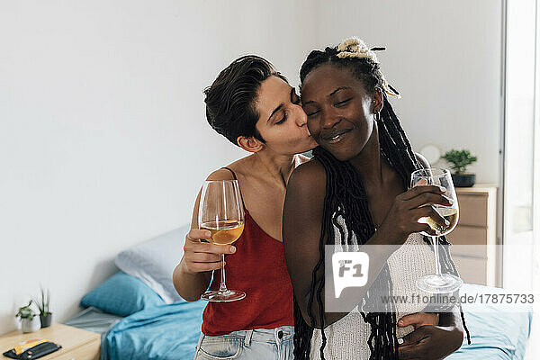 Frau hält Weinglas und küsst Freundin zu Hause